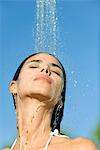 Mid-adult woman under shower outdoors with eyes closed