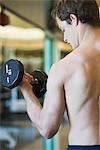 Barechested young man lifting dumbbell, rear view