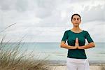 Mature woman in prayer position on beach, portrait