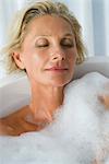 Mature woman relaxing in bubble bath with eyes closed, portrait