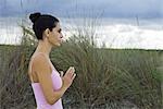 Mature woman in prayer position outdoors, side view