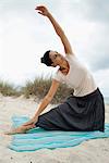 Mature woman doing yoga stretch on beach, portrait