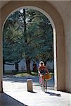 Italy, Tuscany, Lucca. Woman cycling through one of the numerous gates leading to the old city
