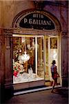 Italy, Tuscany, Lucca. Young woman walking in front of a shop in the historical centre.