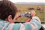 Boy photographing white rhino from a vehicle in Oserian Wildlife Sanctuary, near Lake Naivasha, Kenya.