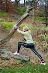 Mature woman stretching against tree in forest