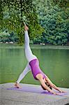 Mid adult woman performing yoga downward dog split pose by river