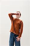 Boy in brown sweater covering eyes, studio shot