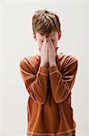 Boy in brown sweater rubbing eyes, studio shot