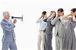 Man yelling in a megaphone at business people with their hands over their ears against white background