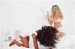 Pillow fight between two attractive women on a white bed