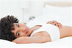 Porträt einer charmanten krauses kurzhaarige Frau liegend auf ihrem Bett vor weißem Hintergrund