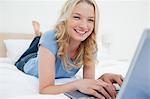 Une femme est allongé sur le lit avec son ordinateur portable, taper loin que dit-elle en souriant, avec ses jambes légèrement croisées.