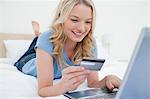 Une femme allongée sur le lit sourit comme elle utilise sa carte de crédit et portable pour la facturation des commandes en ligne.