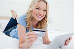 Une femme souriante et regardant droit devant car elle utilise son Tablet PC et la carte de crédit pour acheter des articles.