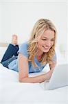 A woman lying on the bed, smiling while using a tablet pc, and looking at the screen.