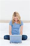 A woman is smiling as she looks at her laptop with her legs folded.