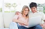 A smiling man and woman sit on the couch as they watch the laptop together.