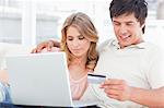 Embracing man and woman use the credit card and laptop together while sitting on the couch.