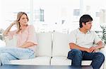 A man looking angry turned the opposite way to the woman at the other end of the couch looking upset.