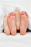 A close up shot of two pairs of feet in between each other in the bed.