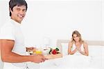 Die Frau und Mann Lächeln beide, wie sie vor ihnen zu suchen, wenn er ihr ein Frühstück im Bett bringt.