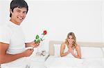 L'homme et la femme sourient en regardant tout droit qu'il lui apporte une rose.