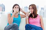 Two women drinking a glass of champagne sitting on a white sofa