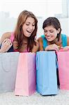 Smiling young women looking at pink and blue shopping bags on the floor