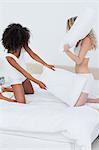 Two teenagers in underwear fighting on a bed with pillows in a bright bedroom