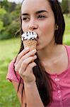 Jeune femme séduisante, regardant de loin tout en mangeant un cornet de crème glacée dans un parc