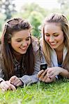 Smiling young girls looking at a text on a cellphone together while lying in a park