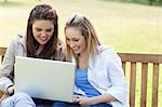 Young happy girls looking at a laptop while sitting on a bench in the countryside