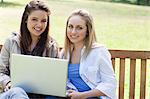 Young girls looking at the camera while holding a laptop and sitting on a bench
