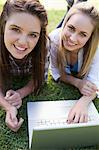 Young girls lying in a public garden while smiling at the camera in front of a laptop