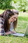 Seitenansicht von jungen Frauen mit einem Laptop beim liegen auf dem Rasen in einem Park