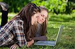 Young calm students lying in the countryside while using a laptop