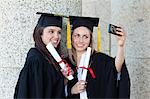 Young graduating students photographing themselves with their gowns and diplomas