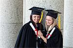 Young happy graduating students holding their diplomas while looking at a camera