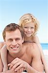 Little boy lying on his fathers back on the beach