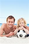 Cheerful souriant père et fils, bronzer sur la plage avec un ballon de football