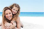 Little girl laying on her mothers back on the beach