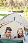The couple lying down in the tent together are looking at something to the side and smiling