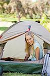 A woman almost fully inside a tent as she smiles with her head just outside the door of it