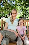 A close up shot of a mother and daughter sitting on the park bench together