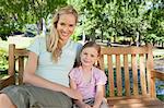 A smiling mother and daughter sitting on the park bench together holding each other