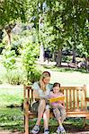 A mother and daughter smiling while sitting on the park bench reading together