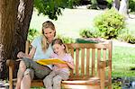 A side view shot of a mom and her child reading a book while they sit on a bench together