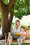 Un plan d'un enfant souriant et sa mère lire un livre ensemble, comme ils sont assis sur le banc rapproché