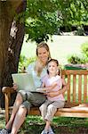 A mother and daughter enjoy the use of a laptop while in the park